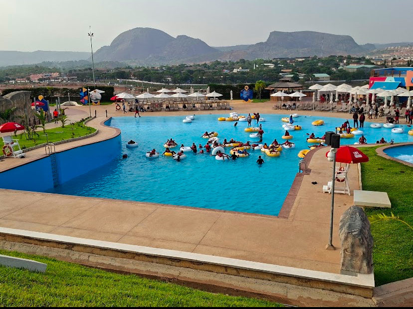 Visitors on floats in the wave pool at Sunrise Water Park with hills behind, Abuja